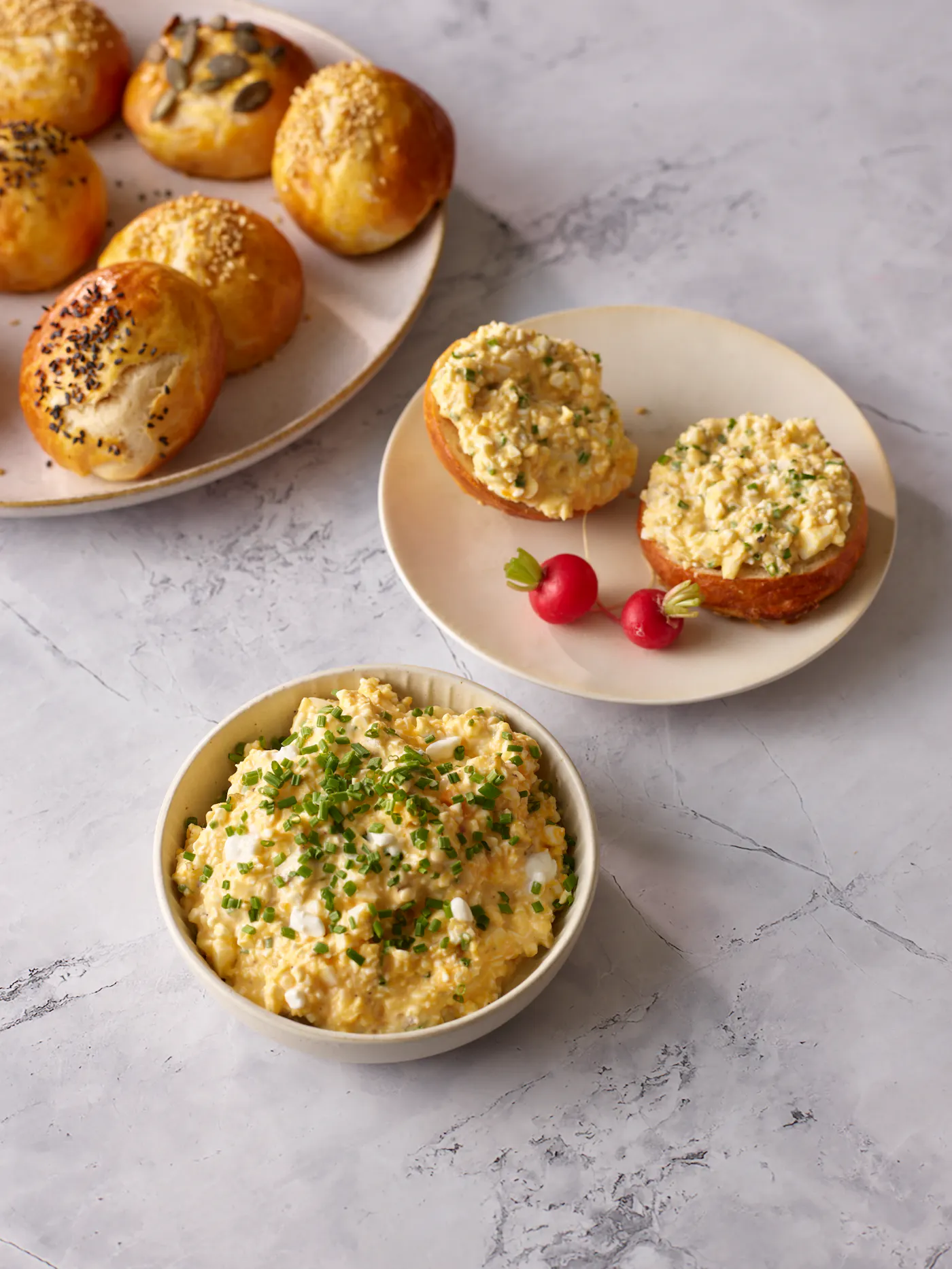 Eiaufstrich in einer hellen Schüssel mit viel Schnittlauch. Im Hintergrund sieht man Laugenweckerl