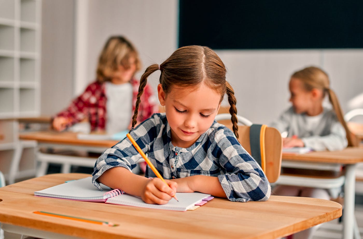 Ein junges Mädchen sitzt in einer Schulklasse und macht Aufgaben an einem Holztisch Ein junges Mädchen sitzt in einer Schulklasse und macht Aufgaben an einem Holztisch