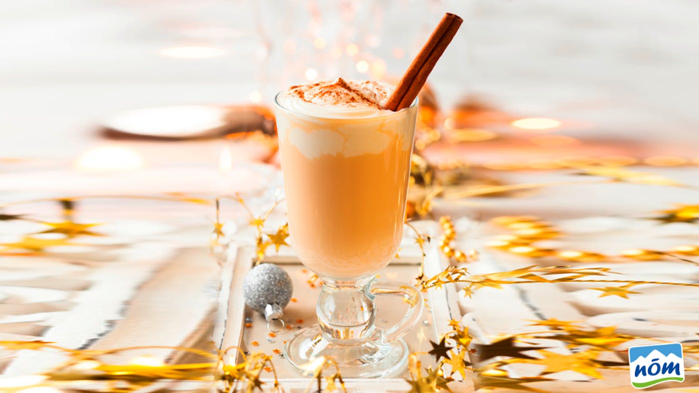 Ein Glas gefüllt mit Schneepunsch auf einem weihnachtlich dekorierten Tisch Ein Glas gefüllt mit Schneepunsch auf einem weihnachtlich dekorierten Tisch