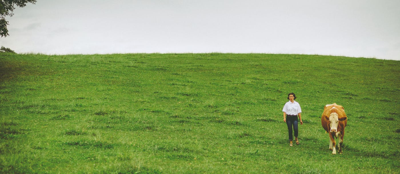 Eine Bäuerin geht neben einer Kuh über eine Weide
