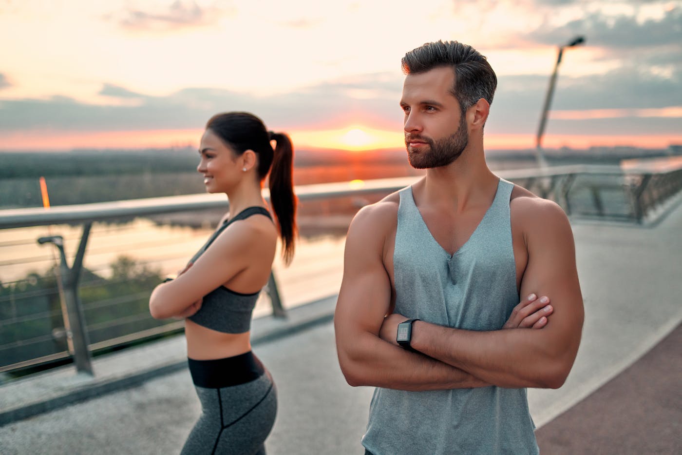 Sportliche Frau und sportlicher Mann stehen auf Brücke im Abendrot