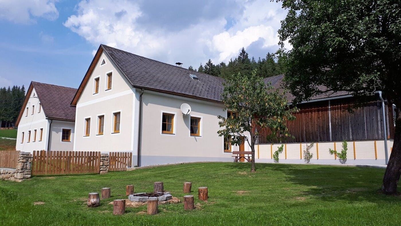 Ferienhaus Buxbaum - Gemütliches Ferienhaus im ländlichen Stil mit hellen Fassaden und Holzakzenten, daneben eine große Wiese mit Feuerstelle, Baum und Holzzaun