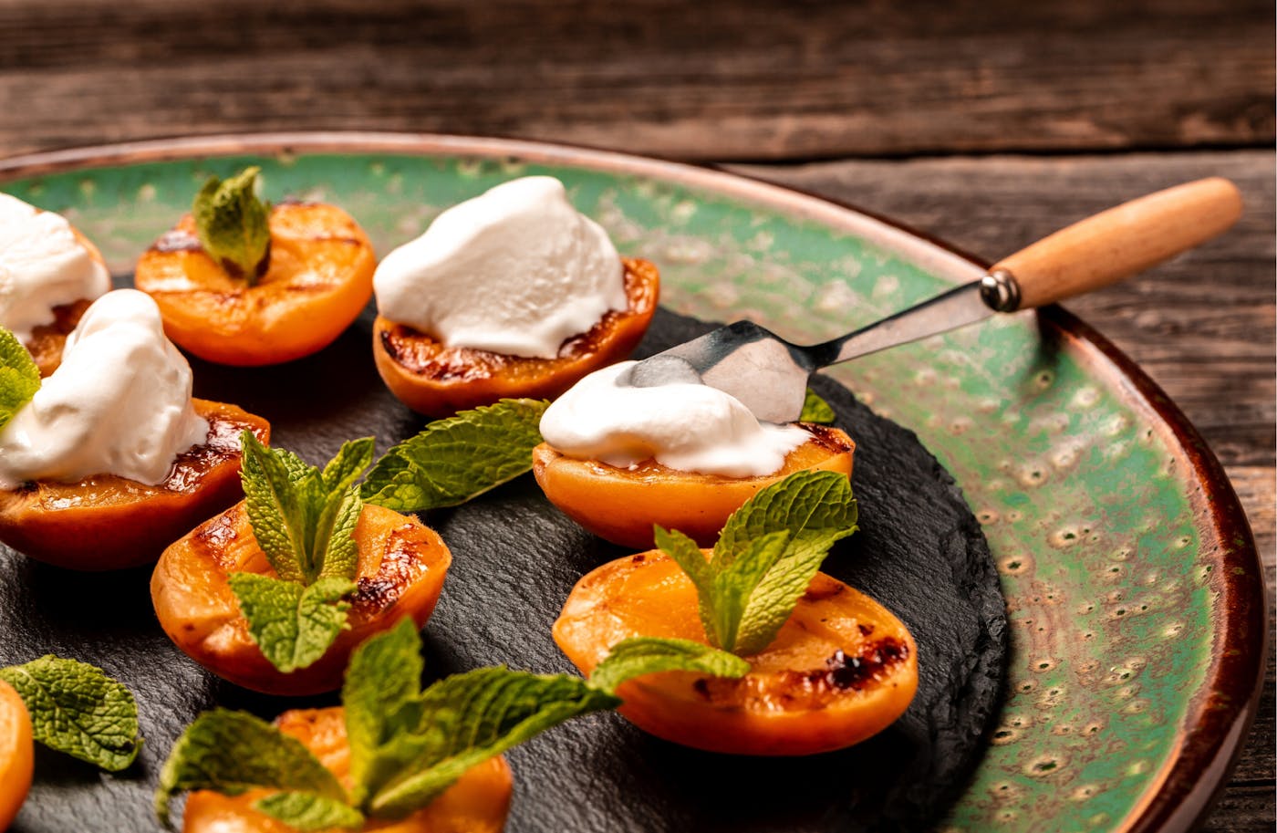 Gegrillte Marille angerichtet mit Joghurt und Kräutern auf grünen Teller Gegrillte Marille angerichtet mit Joghurt und Kräutern auf grünen Teller