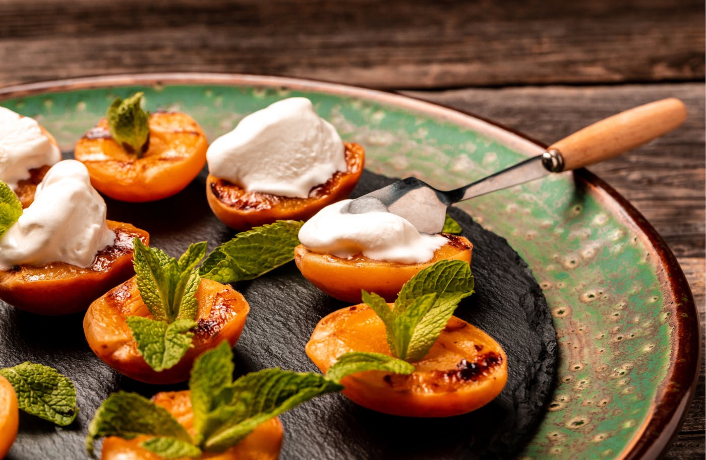 Gegrillte Marille angerichtet mit Joghurt und Kräutern auf grünen Teller