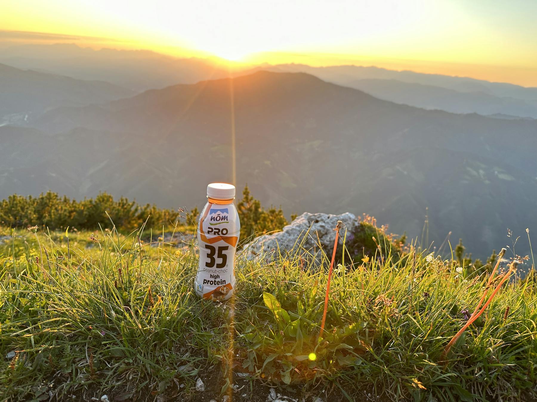 NÖM PRO Drink Peanut-Choc bei Sonnenuntergang mit Alpen-Panorama