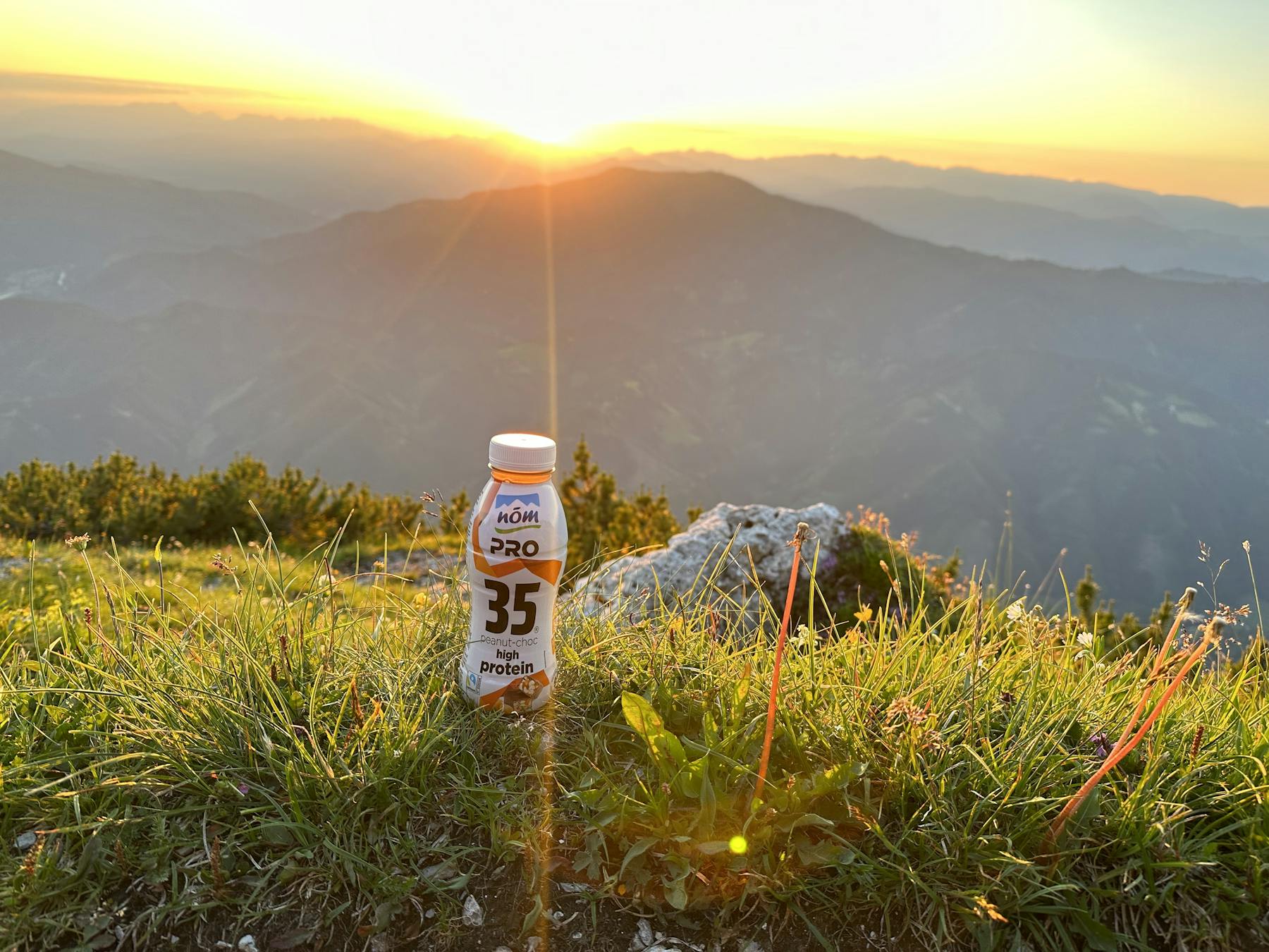 NÖM PRO Drink Peanut-Choc bei Sonnenuntergang mit Alpen-Panorama NÖM PRO Drink Peanut-Choc bei Sonnenuntergang mit Alpen-Panorama