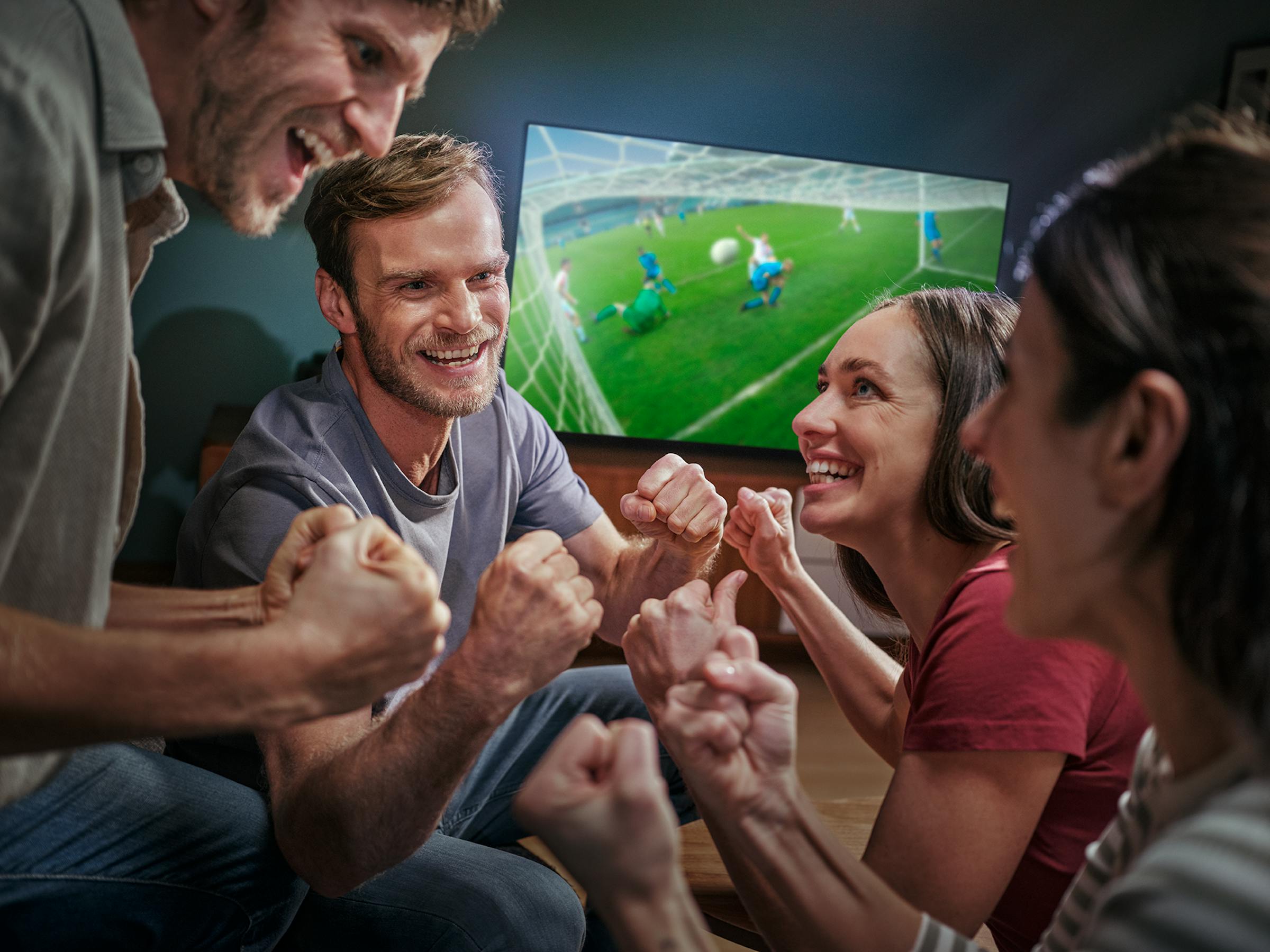 Eine Gruppe junger Erwachsener jubelt bei einem Fußballspiel vor dem Fernseher