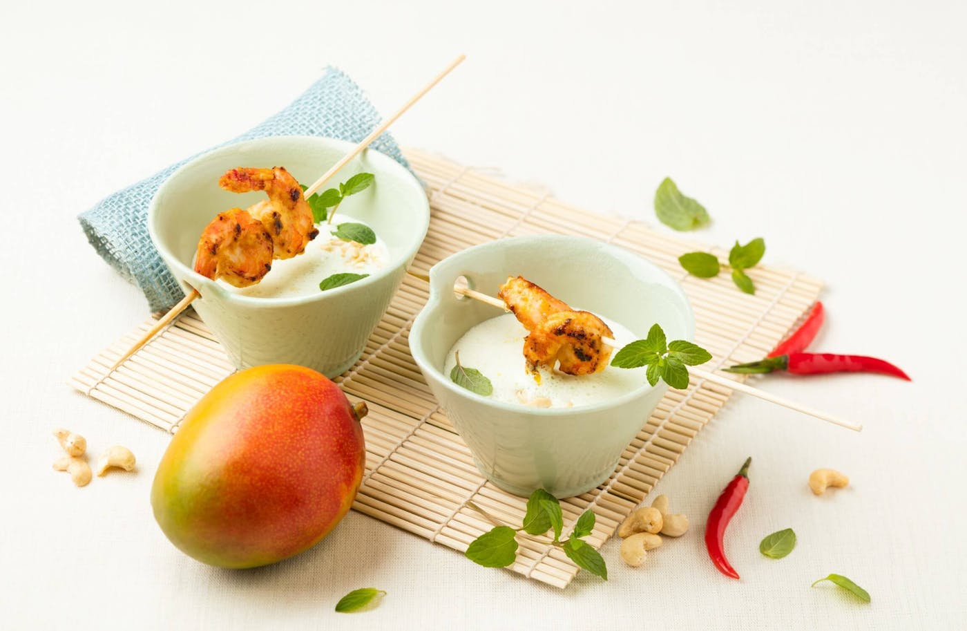Joghurtsuppe Mango Chili Shrimps angerichtet in Schalen auf Bambusmatte mit Mango und Chilischoten