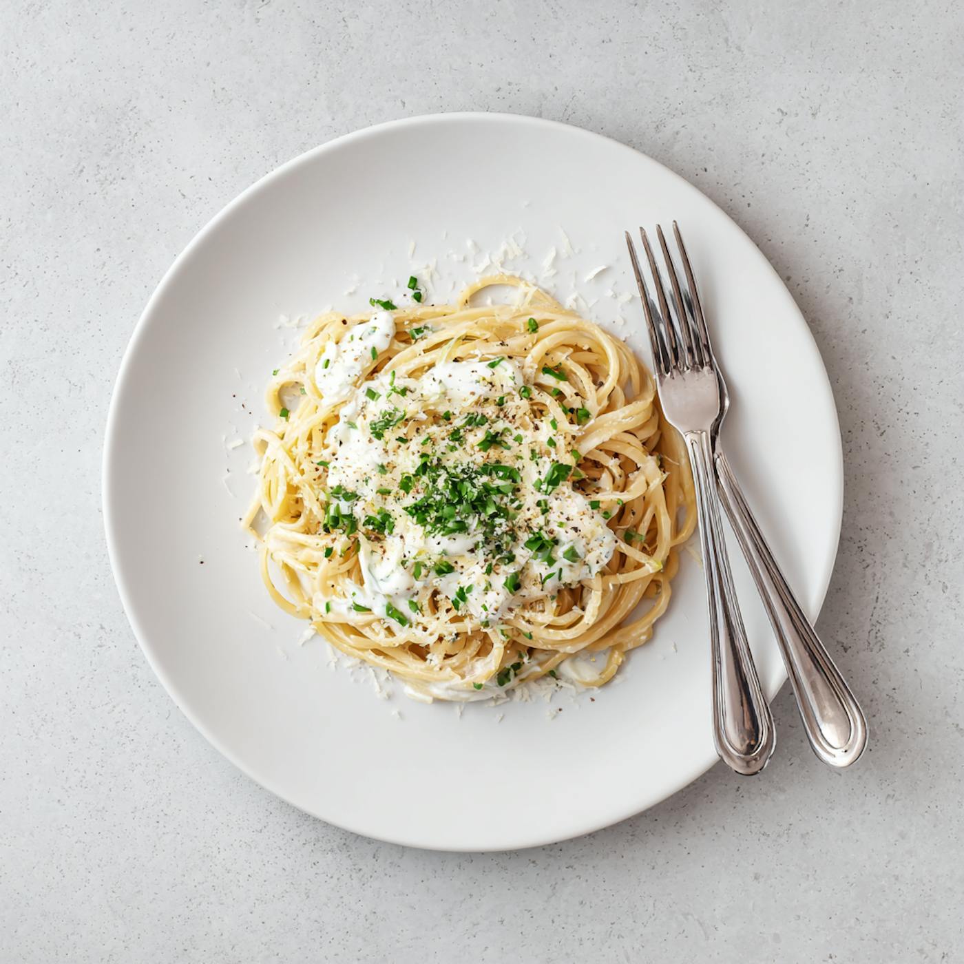 Teller Spaghetti mit weißer Sauce und grünen Kräutern, daneben liegen Gabel und Löffel. Teller Spaghetti mit weißer Sauce und grünen Kräutern, daneben liegen Gabel und Löffel.