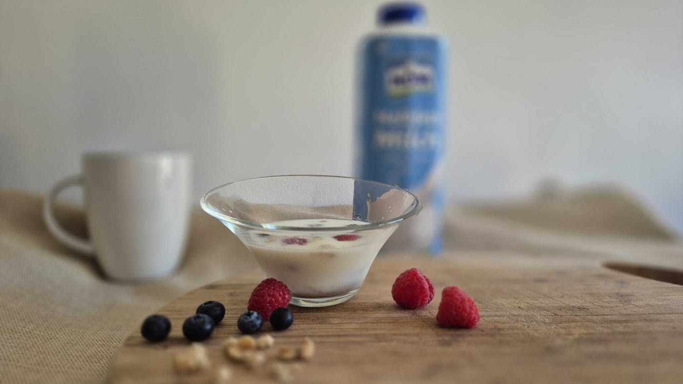 Müslischüssel mit frischen Beeren, einer Tasse und Milch