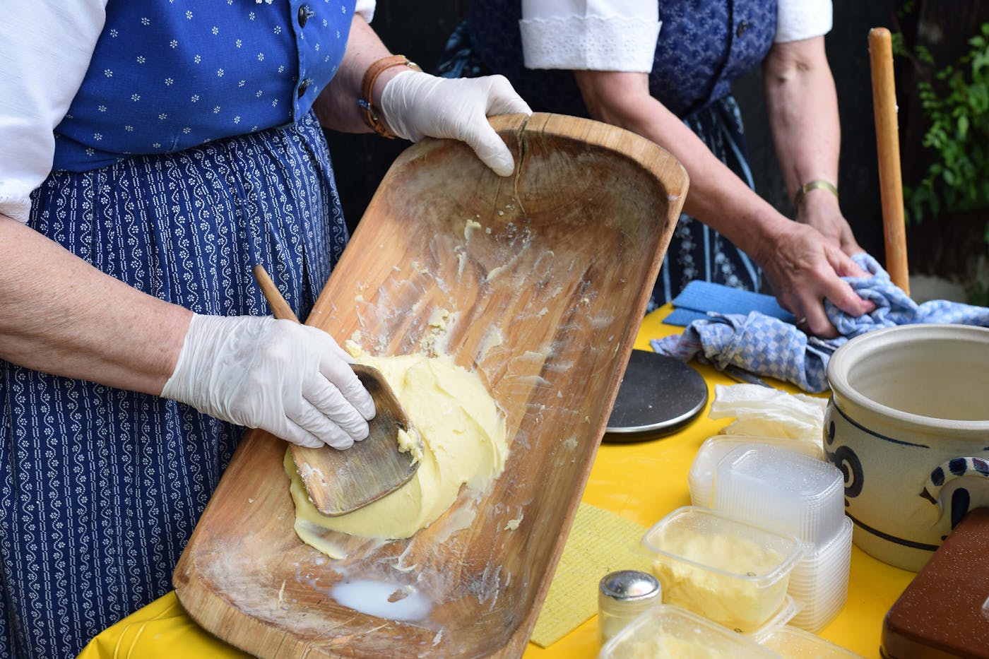 Zwei Bäuerinnen im blauen Dirndl arbeiten gemeinsam an der traditionellen Herstellung von Butter.