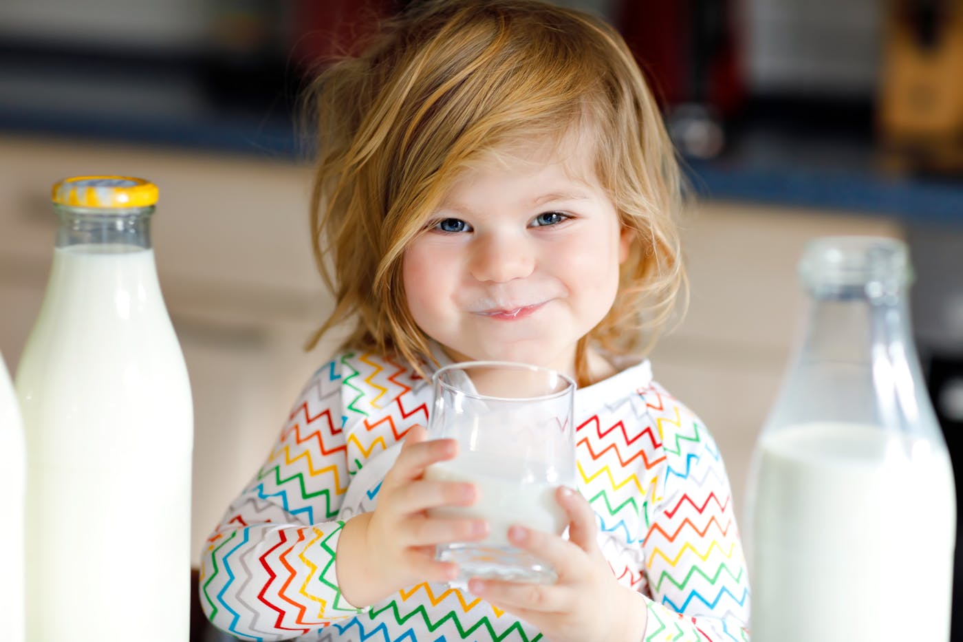 Kleines Mädchen trinkt ein Glas Milch zwischen Milchflaschen