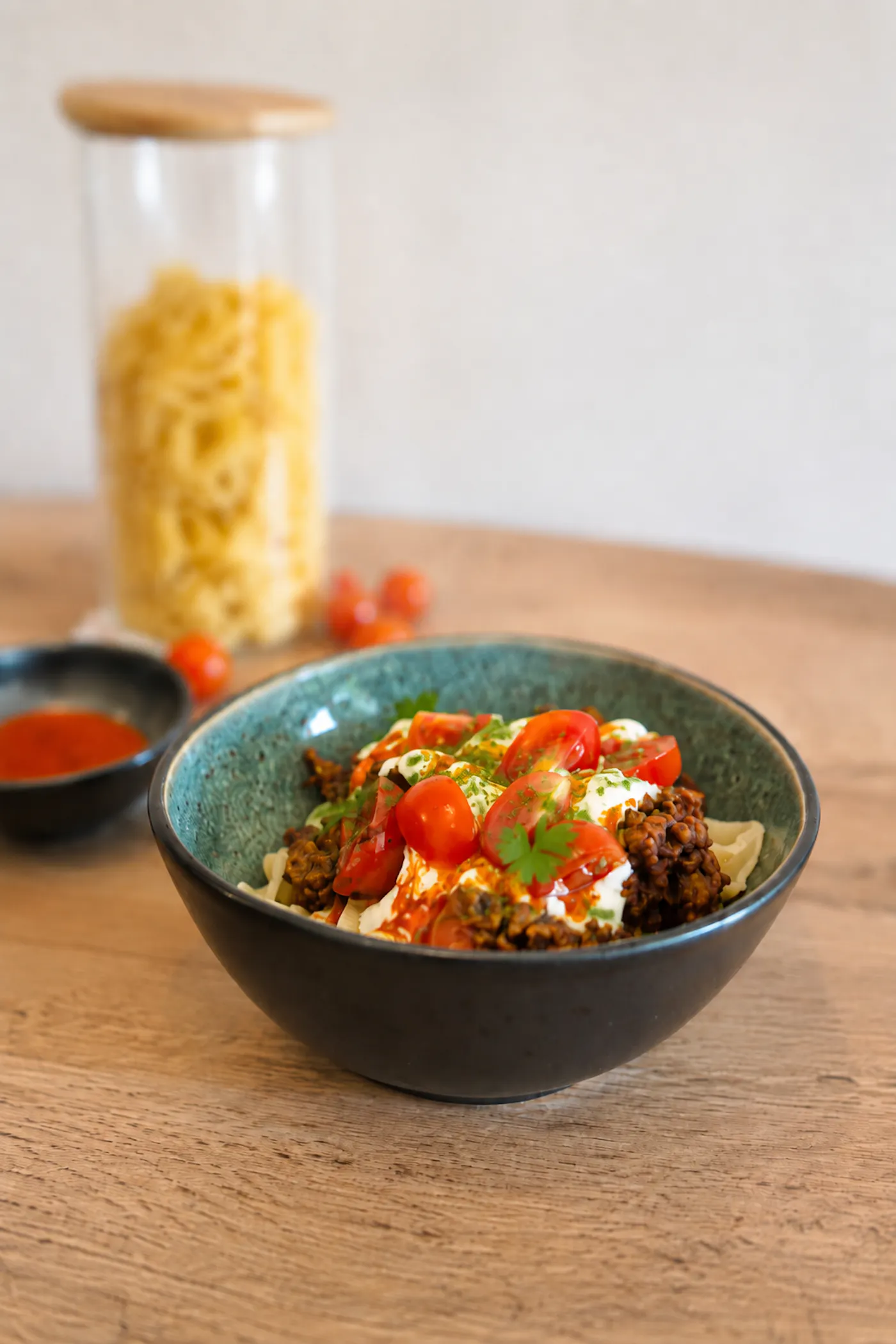 Eine schwarze Schüssel gefüllt mit Fake Manti, frischen Tomaten und frischen Kräutern auf einem Holztisch