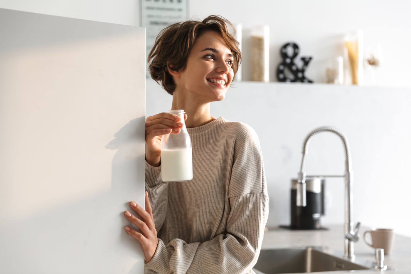 Frau holt Milch in Glasflasche aus dem Kühlschrank