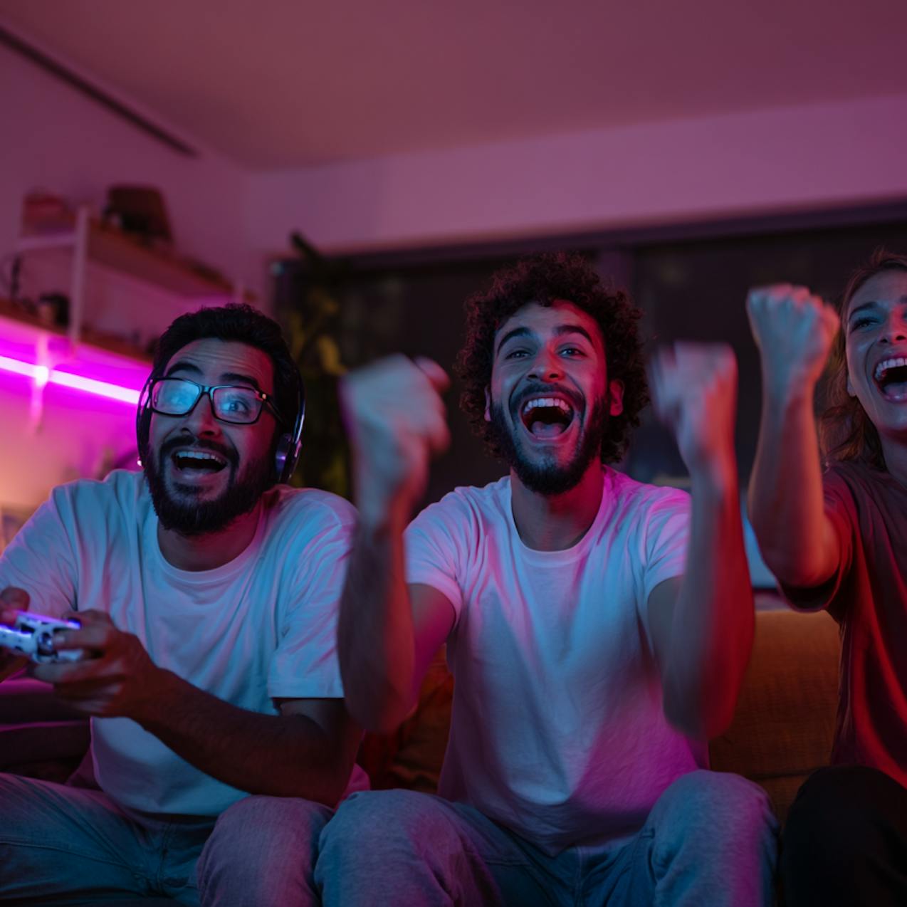 Drei junge Leute bei einem Gaming-Abend jubeln während des Spiels Drei junge Leute bei einem Gaming-Abend jubeln während des Spiels