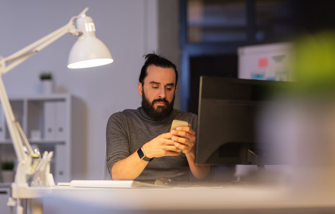 Hipper junger Mann sitzt gestresst vor PC und Smartphone