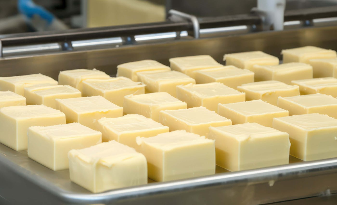 Frisch produzierte Butterwürfel liegen geordnet auf einem glänzenden Metalltablett, das Teil einer industriellen Butterherstellungsmaschine ist.