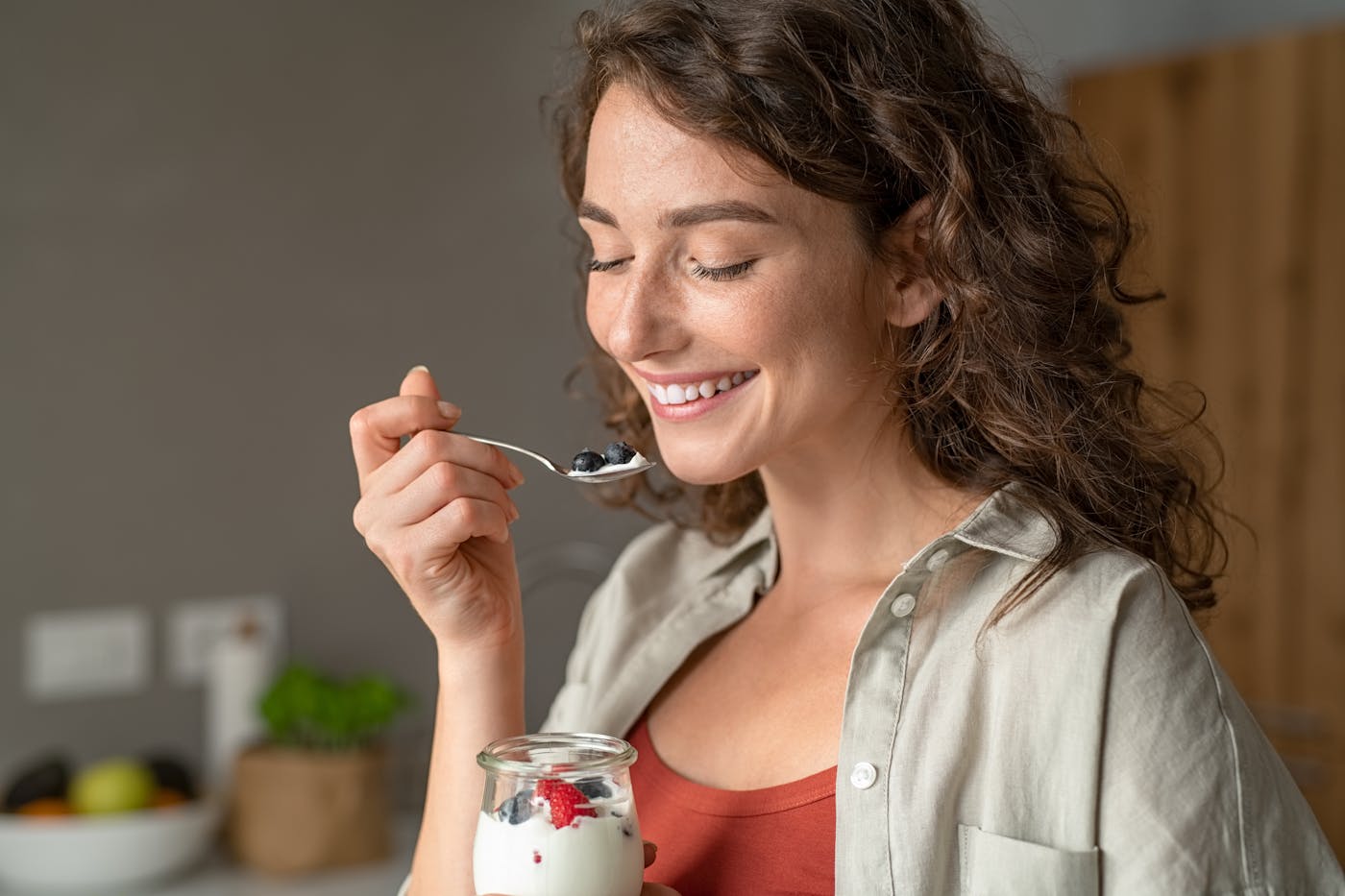 Junge Frau isst Joghurt mit Beeren aus einem Gläschen