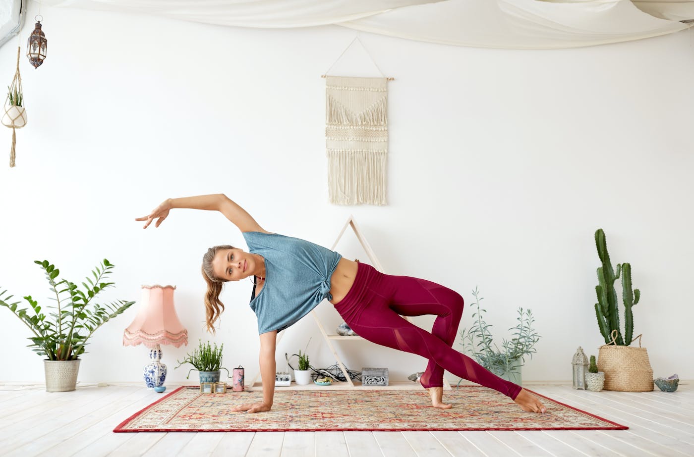 Junge fitte Frau praktiziert Yoga auf buntem Teppich in hellem Studio