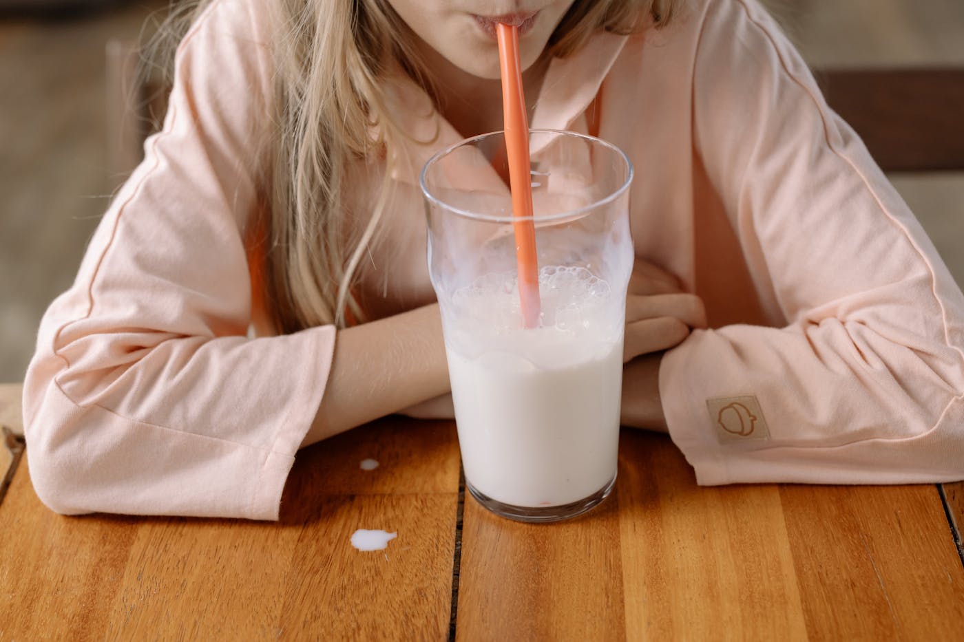 Mädchen trinkt Milch mit einem Strohhalm aus einem Glas