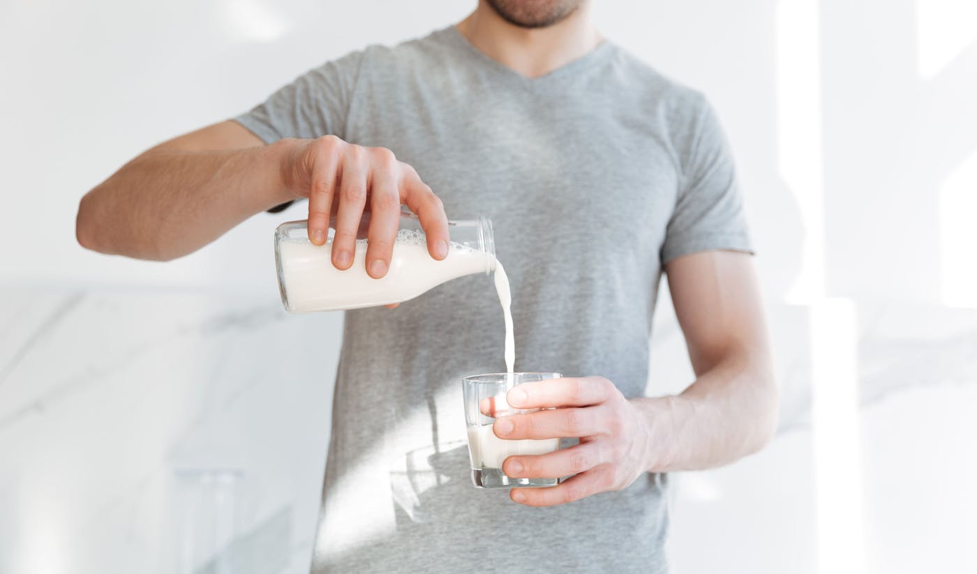 Mann schenkt Milch aus Glasflasche in ein Glas