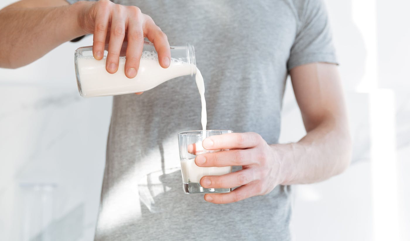 Mann schenkt Milch aus Glasflasche in ein Glas