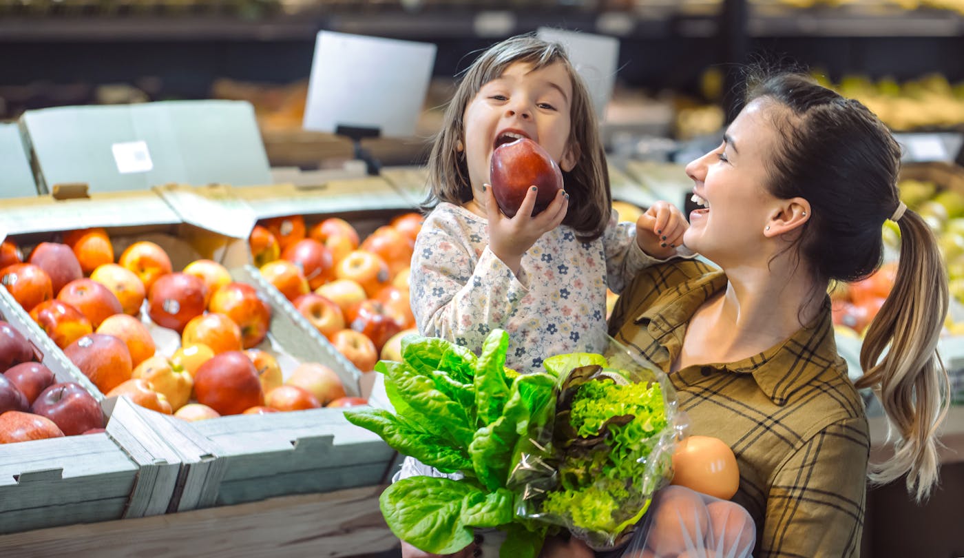 Junge Mutter mit lachender Tochter beim Lebensmittelkauf im Supermarkt in der Obstabteilung