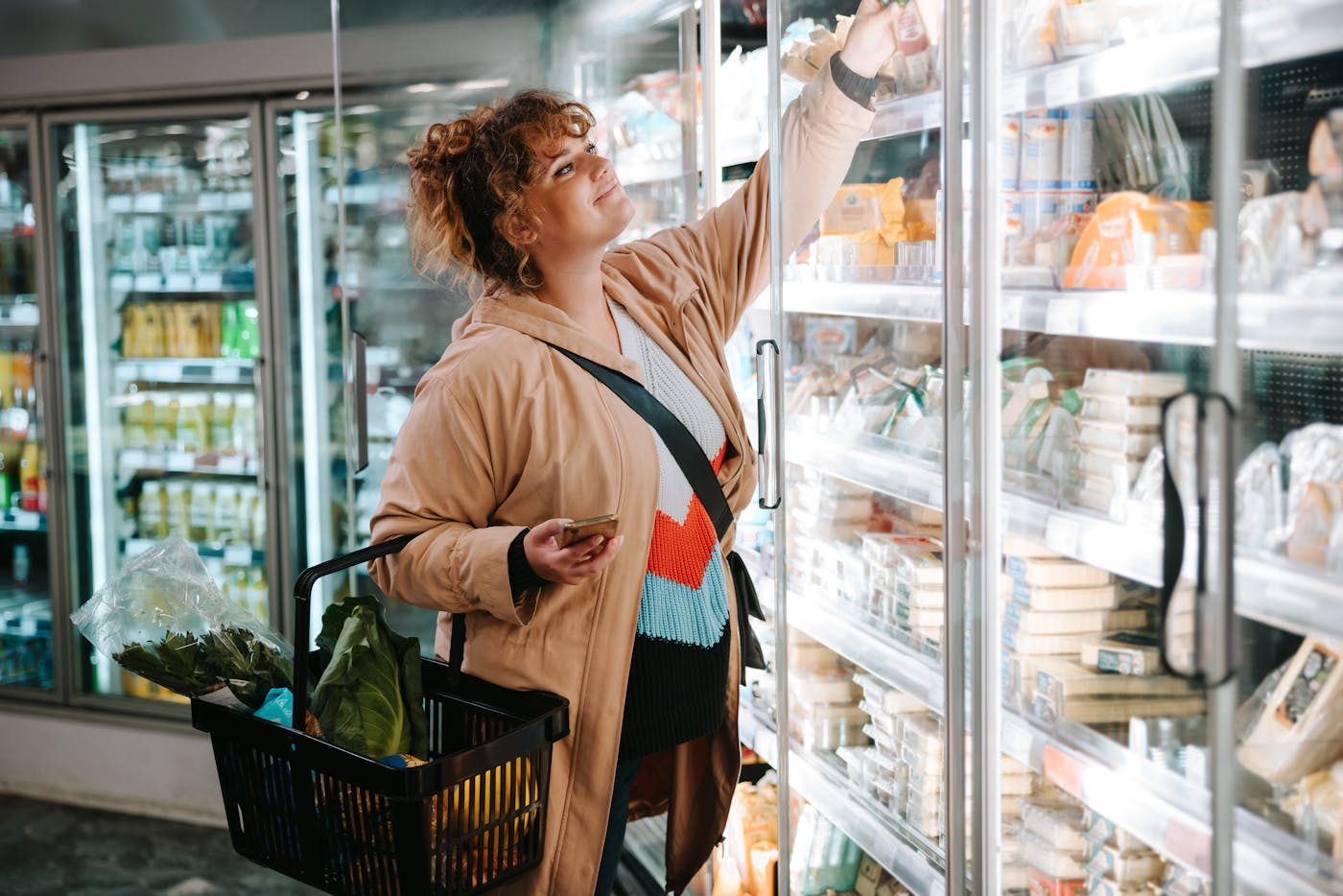 Frau beim Lebensmitteleinkauf im Supermarkt steht vor dem Kühlregal mit Milchprodukten