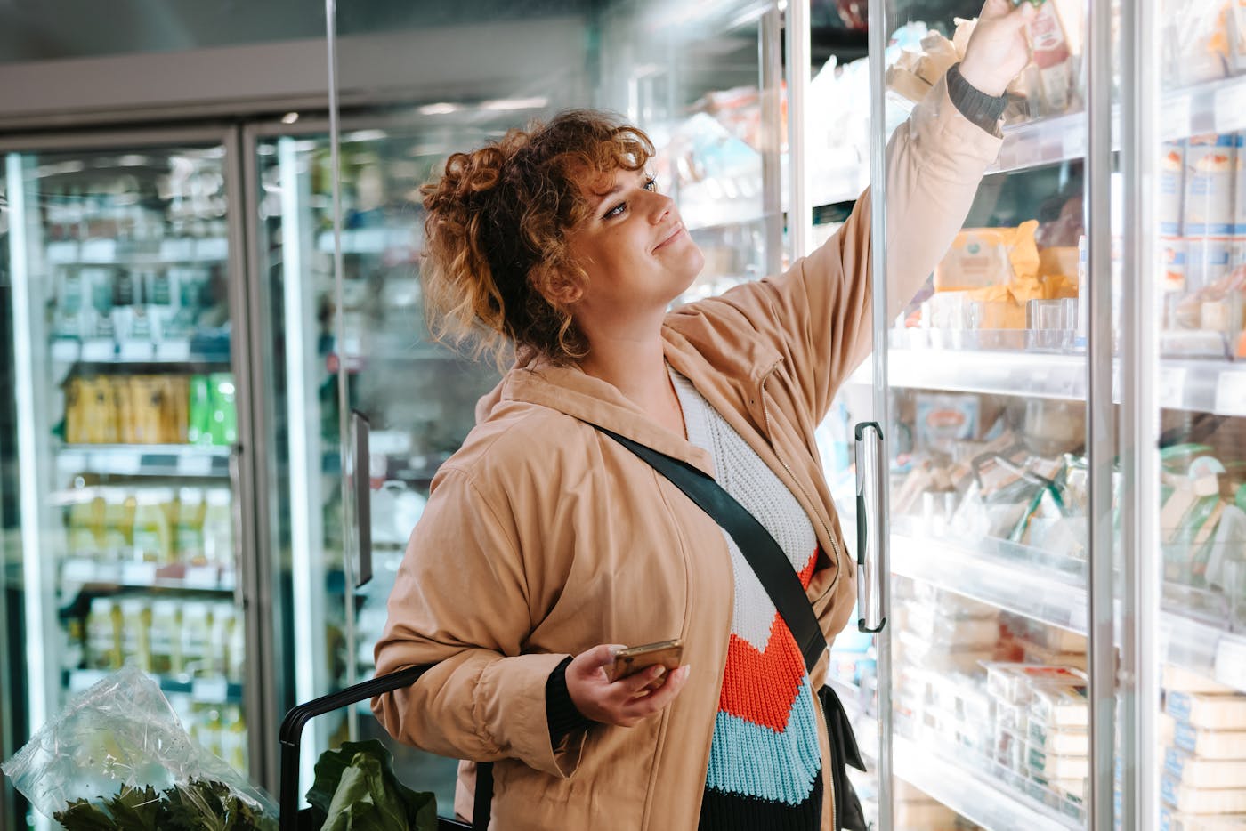 Frau beim Lebensmitteleinkauf im Supermarkt steht vor dem Kühlregal mit Milchprodukten