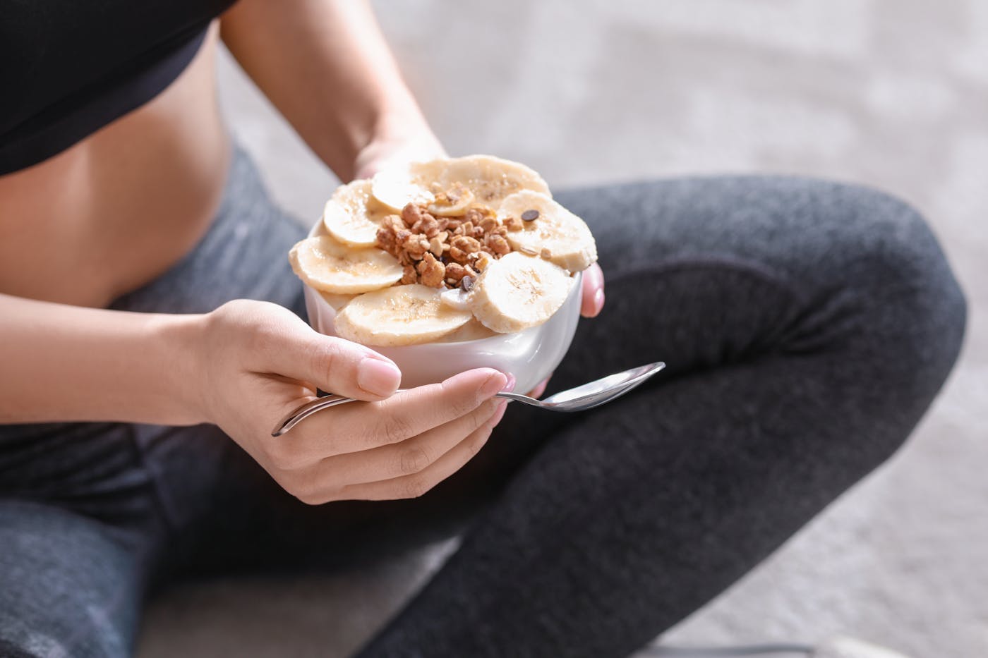 Sportliche Frau isst proteinreichen Joghurt und sitzt im Schneidersitz auf dem Boden